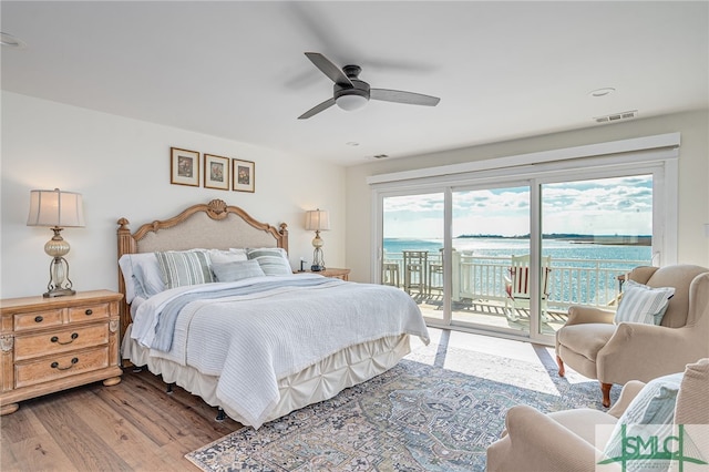 bedroom featuring access to exterior, wood-type flooring, ceiling fan, and a water view