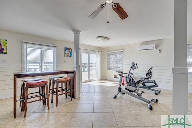 exercise area with ornate columns, a wall mounted AC, light tile patterned floors, and ceiling fan