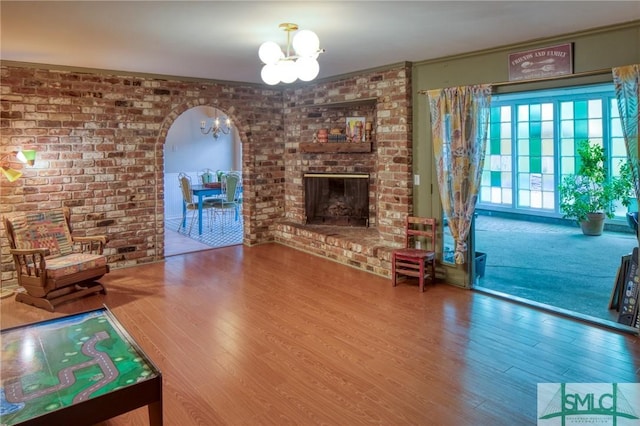 living room featuring crown molding, wood-type flooring, brick wall, a brick fireplace, and a chandelier