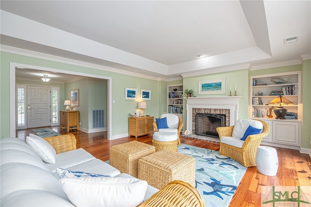 living room featuring a fireplace, wood-type flooring, a tray ceiling, and built in features