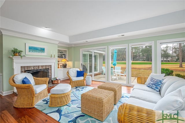 living room with built in shelves, wood-type flooring, a fireplace, and crown molding