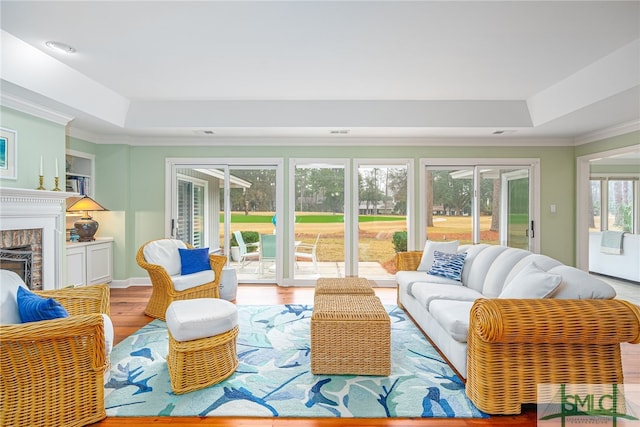 living room featuring crown molding, a brick fireplace, a tray ceiling, and hardwood / wood-style floors