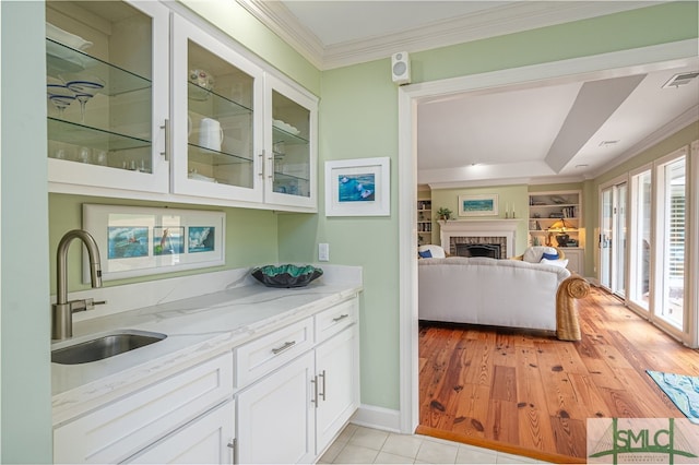 kitchen featuring sink, white cabinetry, crown molding, light stone counters, and built in features