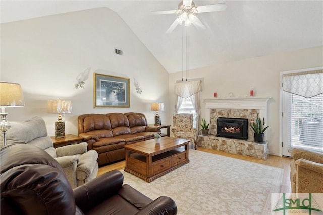 living room with ceiling fan, high vaulted ceiling, a fireplace, and light hardwood / wood-style floors