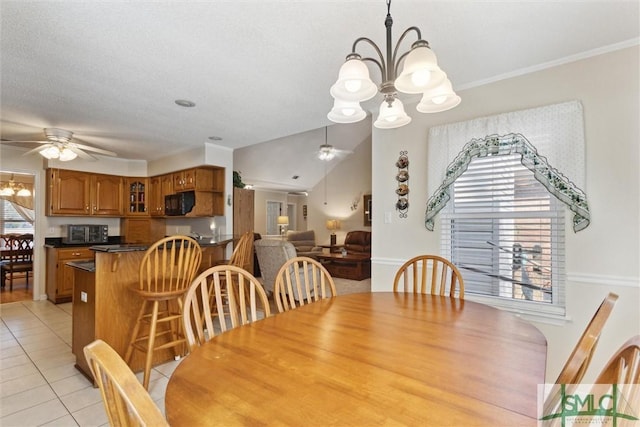 tiled dining space featuring crown molding, lofted ceiling, and ceiling fan with notable chandelier