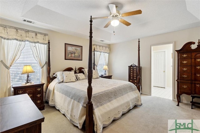 bedroom with light colored carpet, a raised ceiling, and ceiling fan