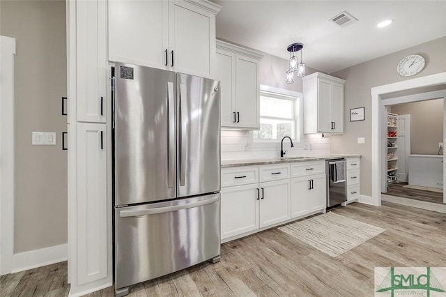 kitchen with sink, light hardwood / wood-style flooring, appliances with stainless steel finishes, white cabinetry, and light stone countertops