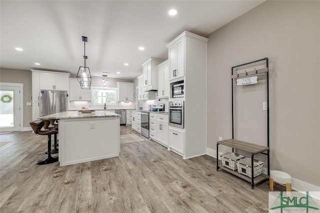 kitchen with appliances with stainless steel finishes, a center island, white cabinets, and decorative light fixtures