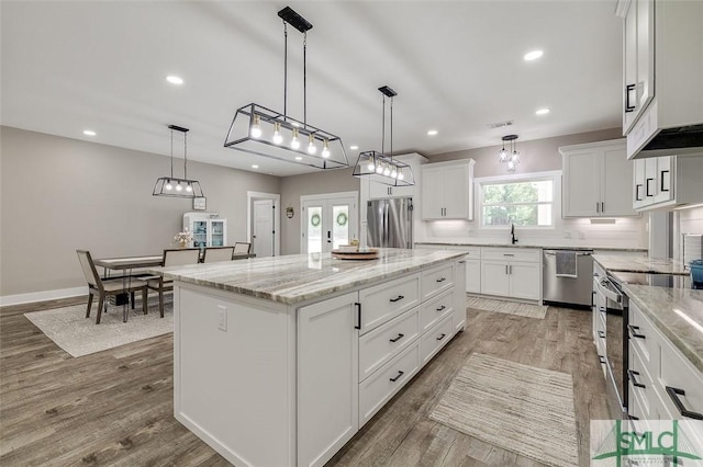 kitchen featuring stainless steel appliances, light stone counters, white cabinets, a kitchen island, and decorative light fixtures