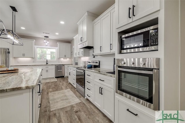 kitchen with white cabinetry, hanging light fixtures, light stone counters, and appliances with stainless steel finishes