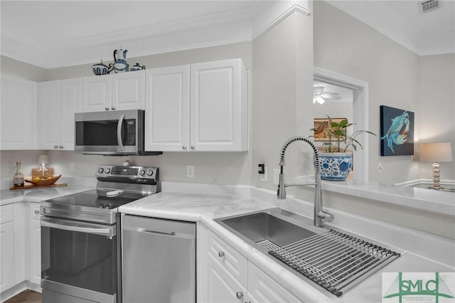 kitchen featuring appliances with stainless steel finishes, sink, white cabinets, ceiling fan, and crown molding