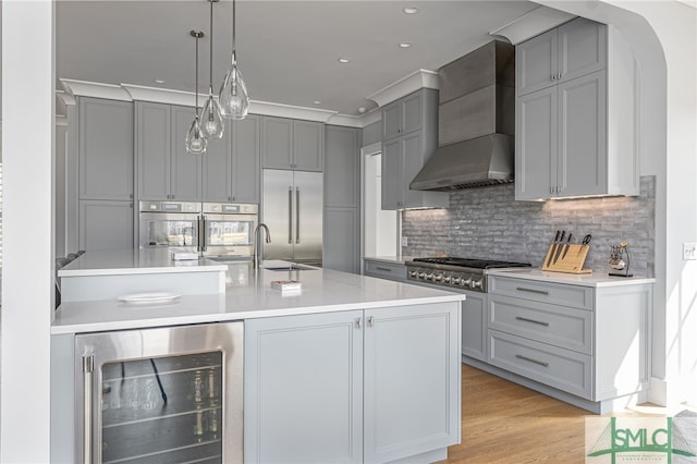 kitchen featuring pendant lighting, gray cabinetry, stainless steel appliances, wine cooler, and wall chimney exhaust hood