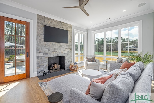 living room with ornamental molding, a stone fireplace, a wealth of natural light, and light wood-type flooring