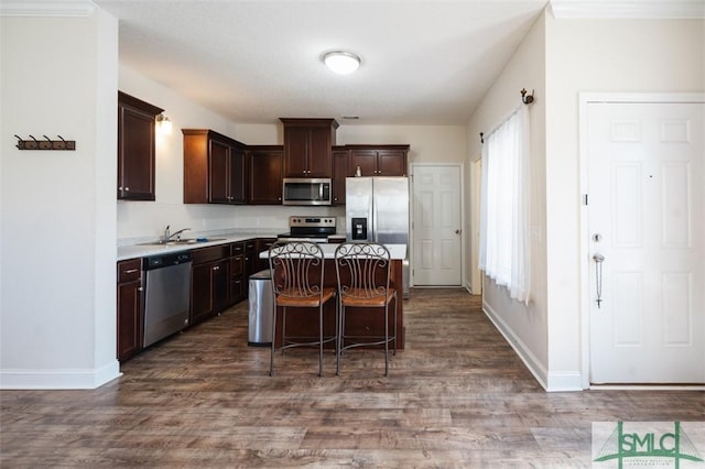 kitchen with a breakfast bar area, appliances with stainless steel finishes, a center island, dark brown cabinetry, and wood-type flooring