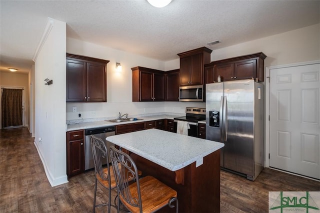 kitchen with a breakfast bar, sink, dark hardwood / wood-style floors, a kitchen island, and stainless steel appliances