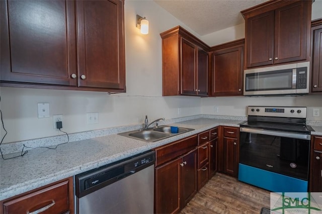 kitchen featuring sink, appliances with stainless steel finishes, light stone countertops, a textured ceiling, and light wood-type flooring