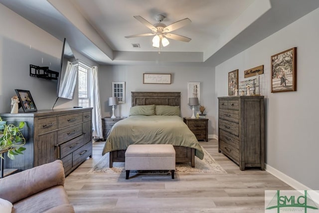 bedroom with ceiling fan, a raised ceiling, and light hardwood / wood-style floors