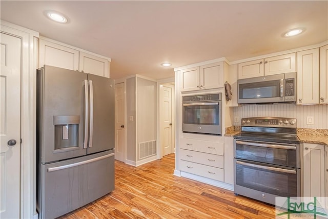 kitchen with appliances with stainless steel finishes, white cabinets, light stone counters, and light hardwood / wood-style flooring