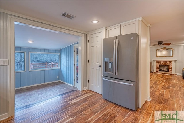 kitchen featuring hardwood / wood-style floors, white cabinets, ceiling fan, stainless steel fridge with ice dispenser, and a brick fireplace