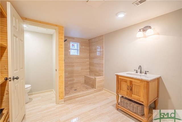 bathroom with hardwood / wood-style flooring, vanity, tiled shower, and toilet