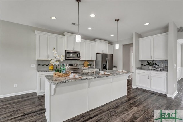 kitchen with appliances with stainless steel finishes, hanging light fixtures, light stone countertops, an island with sink, and white cabinets