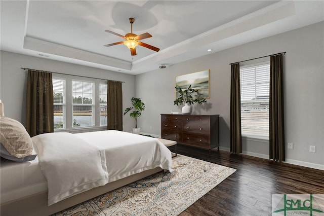 bedroom with ceiling fan, dark hardwood / wood-style flooring, and a raised ceiling