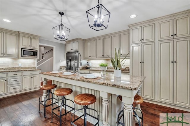 kitchen with a breakfast bar, decorative light fixtures, a center island with sink, stainless steel microwave, and dark hardwood / wood-style flooring