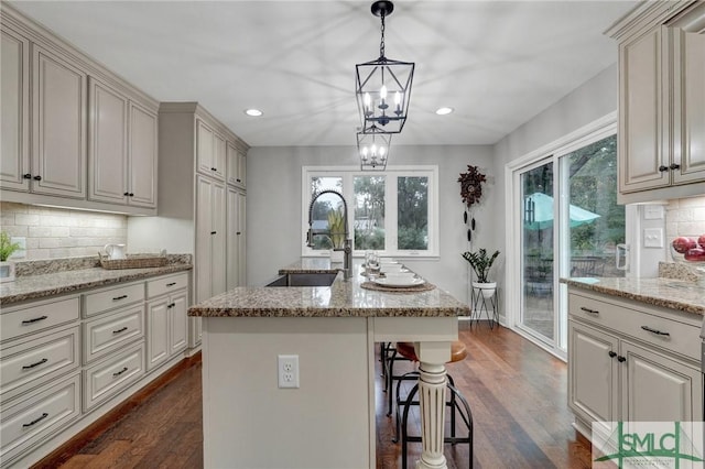 kitchen featuring dark hardwood / wood-style floors, sink, hanging light fixtures, light stone counters, and a center island with sink