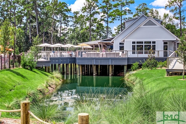 rear view of house with a deck with water view and a yard