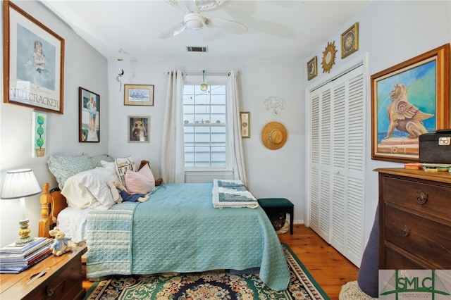 bedroom with a ceiling fan, wood finished floors, visible vents, and a closet