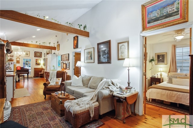 living area with ceiling fan with notable chandelier, beamed ceiling, light wood-style flooring, and high vaulted ceiling