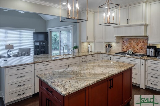 kitchen featuring sink, hanging light fixtures, a center island, decorative backsplash, and stainless steel gas stovetop