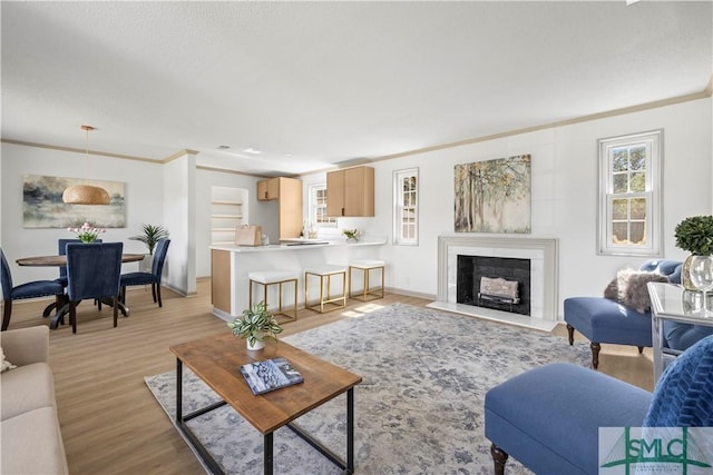 living area featuring a fireplace with flush hearth, baseboards, crown molding, and light wood finished floors