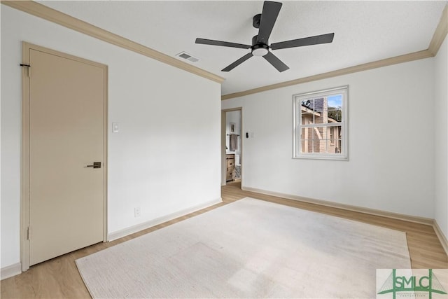 empty room with ornamental molding, light wood-type flooring, visible vents, and baseboards