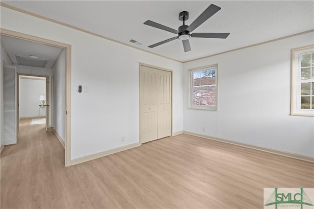 unfurnished bedroom featuring attic access, light wood-style floors, visible vents, and ornamental molding