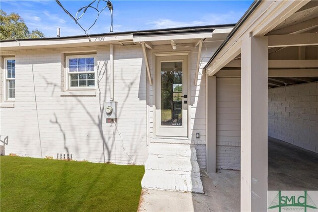 view of exterior entry featuring brick siding and a lawn