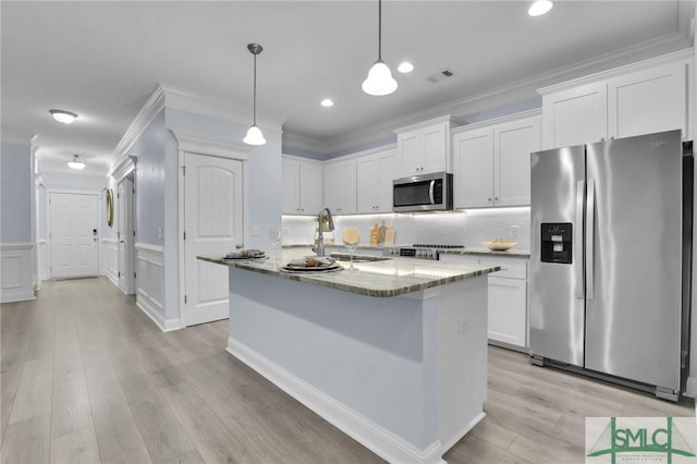 kitchen featuring a kitchen island with sink, hanging light fixtures, stainless steel appliances, and white cabinets