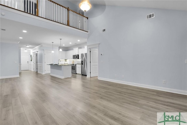 unfurnished living room featuring ornamental molding, sink, a high ceiling, and light wood-type flooring