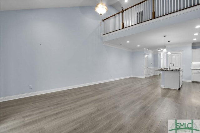 unfurnished living room featuring a towering ceiling, ornamental molding, sink, and light wood-type flooring