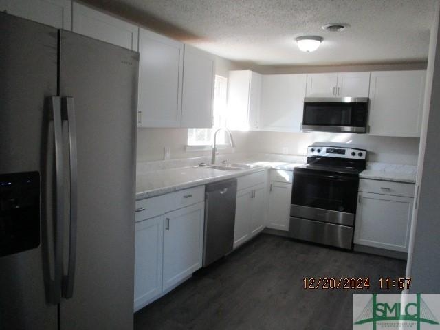 kitchen with sink, dark wood-type flooring, white cabinetry, stainless steel appliances, and a textured ceiling