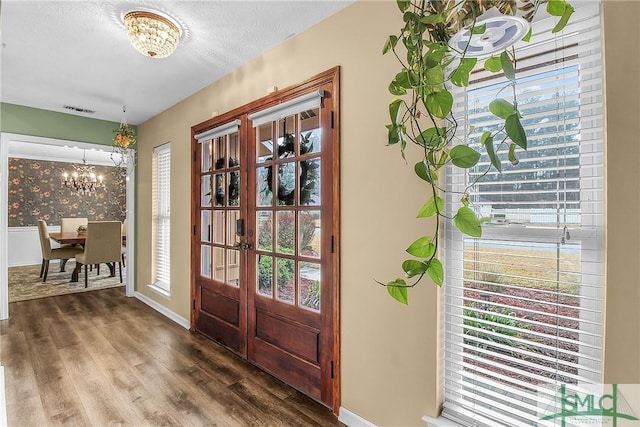 foyer entrance featuring plenty of natural light, dark wood-type flooring, a notable chandelier, and french doors