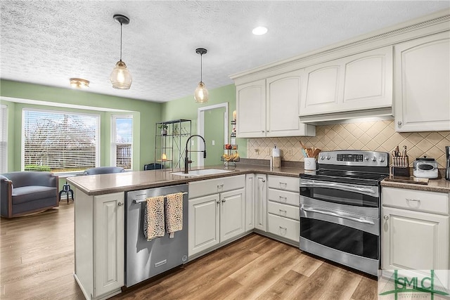 kitchen with sink, appliances with stainless steel finishes, white cabinets, decorative light fixtures, and kitchen peninsula