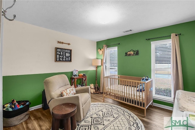 bedroom with a nursery area, dark wood-type flooring, and a textured ceiling