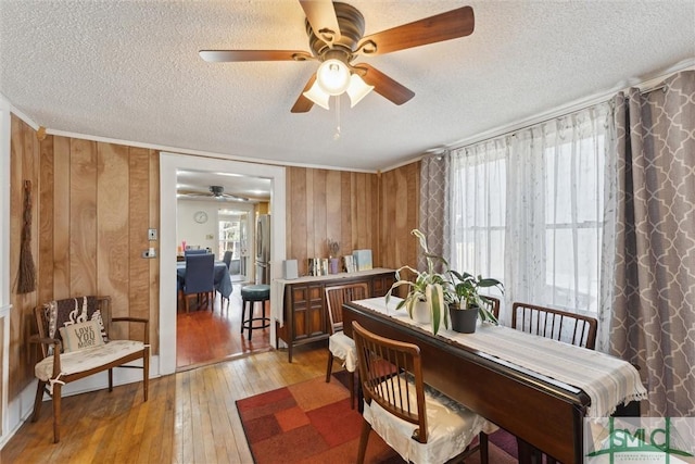 dining space with light hardwood / wood-style floors, crown molding, wood walls, and a textured ceiling