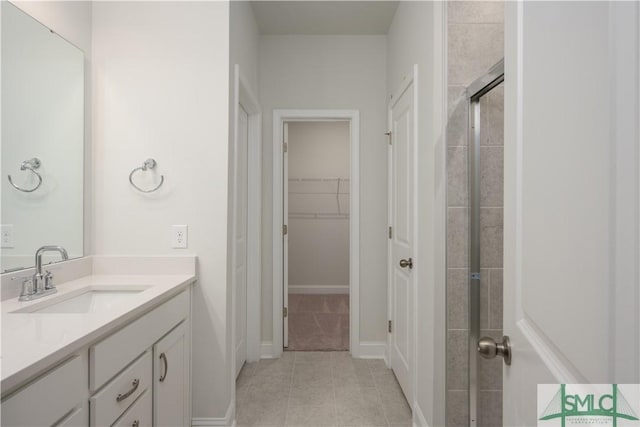 bathroom with vanity, baseboards, a tile shower, tile patterned flooring, and a walk in closet