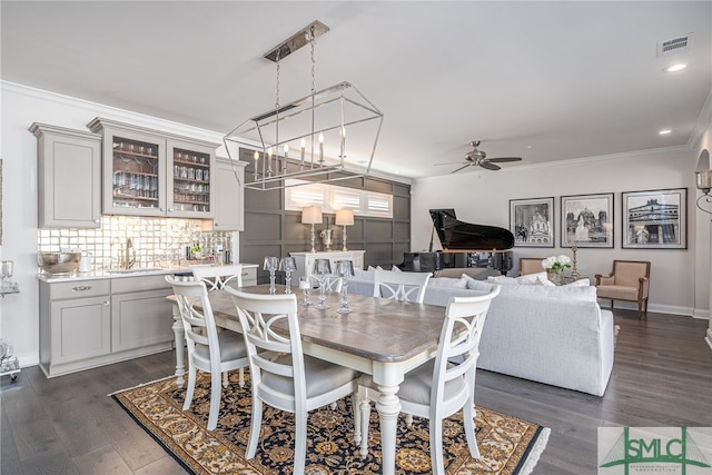 dining space featuring ceiling fan with notable chandelier, sink, dark wood-type flooring, and ornamental molding