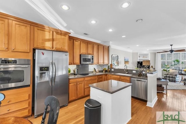 kitchen featuring appliances with stainless steel finishes, sink, backsplash, light hardwood / wood-style flooring, and kitchen peninsula