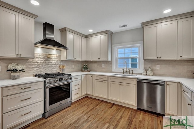 kitchen with appliances with stainless steel finishes, sink, light hardwood / wood-style flooring, wall chimney range hood, and tasteful backsplash