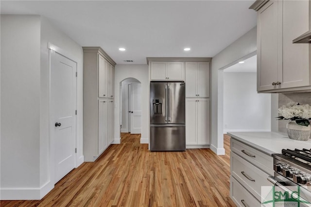 kitchen featuring light hardwood / wood-style flooring, gray cabinetry, high end appliances, wall chimney exhaust hood, and decorative backsplash