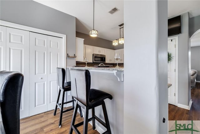 kitchen with backsplash, light stone counters, white cabinetry, pendant lighting, and hardwood / wood-style flooring